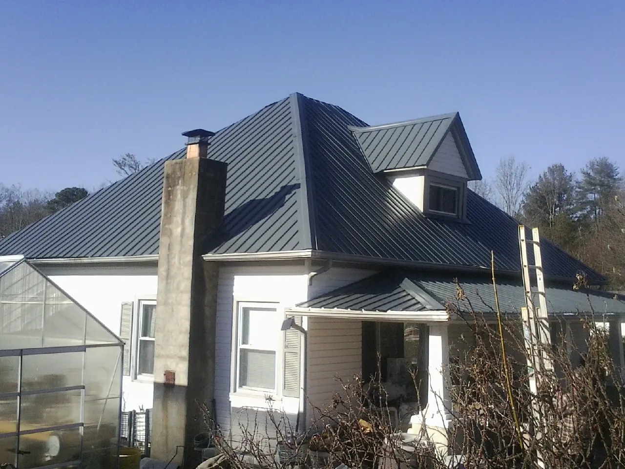 Dark blue standing seam metal roof on a white farmhouse with dormer — Slate & Tile Roof Repair by Roofing Brothers in Rolling Prairie