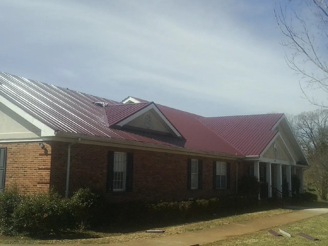 Red metal roof with gabled entries on a long brick building, from a Hail Damage Roof Repair job in Rolling Prairie
