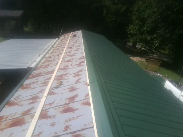 Old rusted panels beside newly installed green metal roofing — Wind Damage Roof Repair by Roofing Brothers in Rolling Prairie