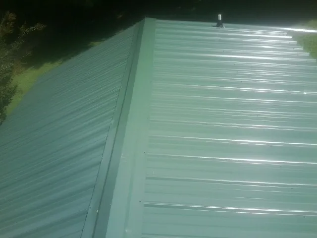 New green metal panels meeting at the ridge of a roof — Flat Roof Repair work by our crew in Rolling Prairie