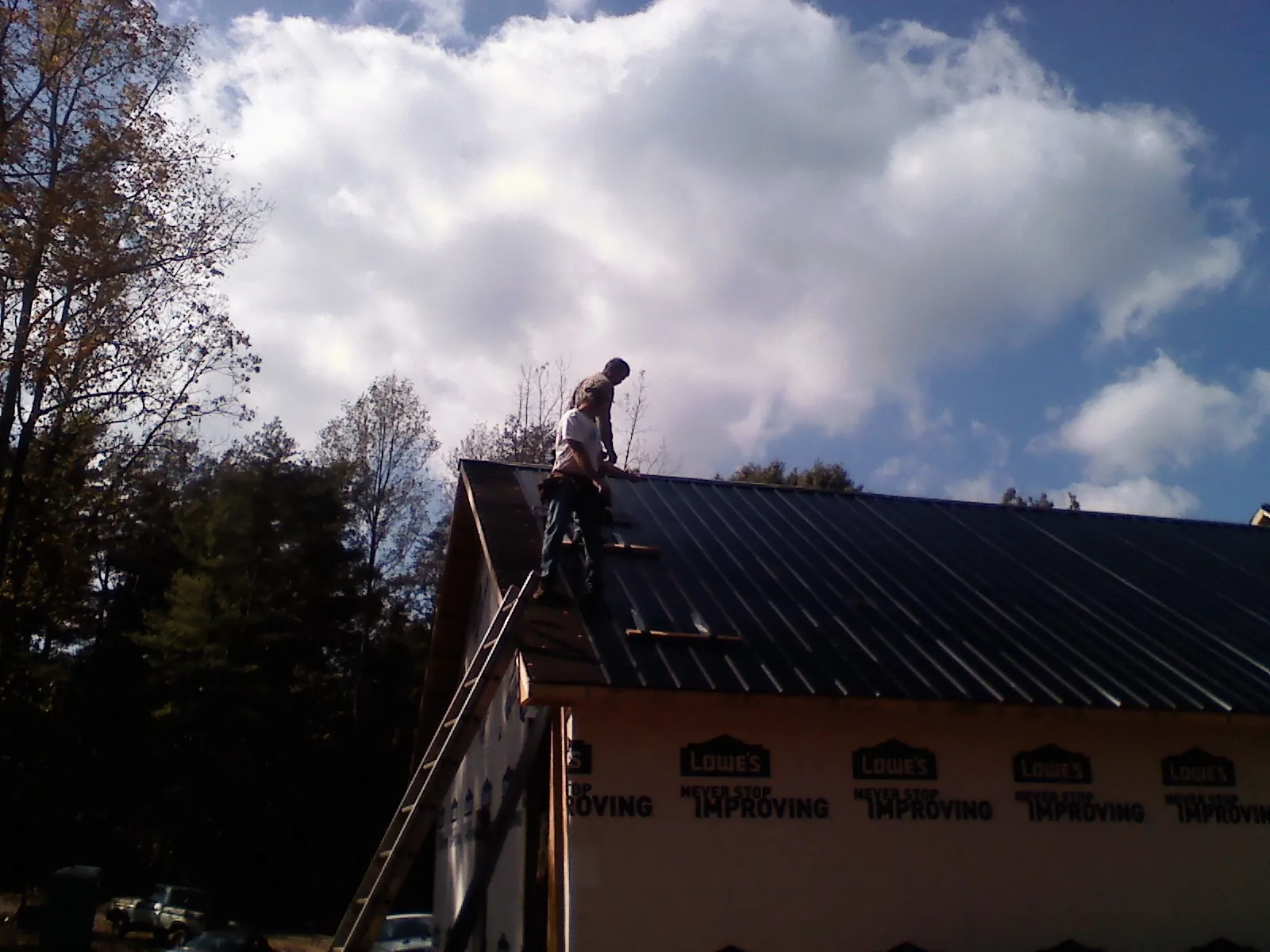 Roofer fastening dark metal panels high against a cloudy sky, from a Roof Inspection job in Rolling Prairie