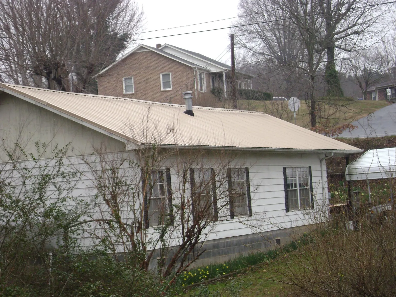 Tan metal roof on a white sided house set into a hillside — Commercial Roofing by Roofing Brothers in Rolling Prairie