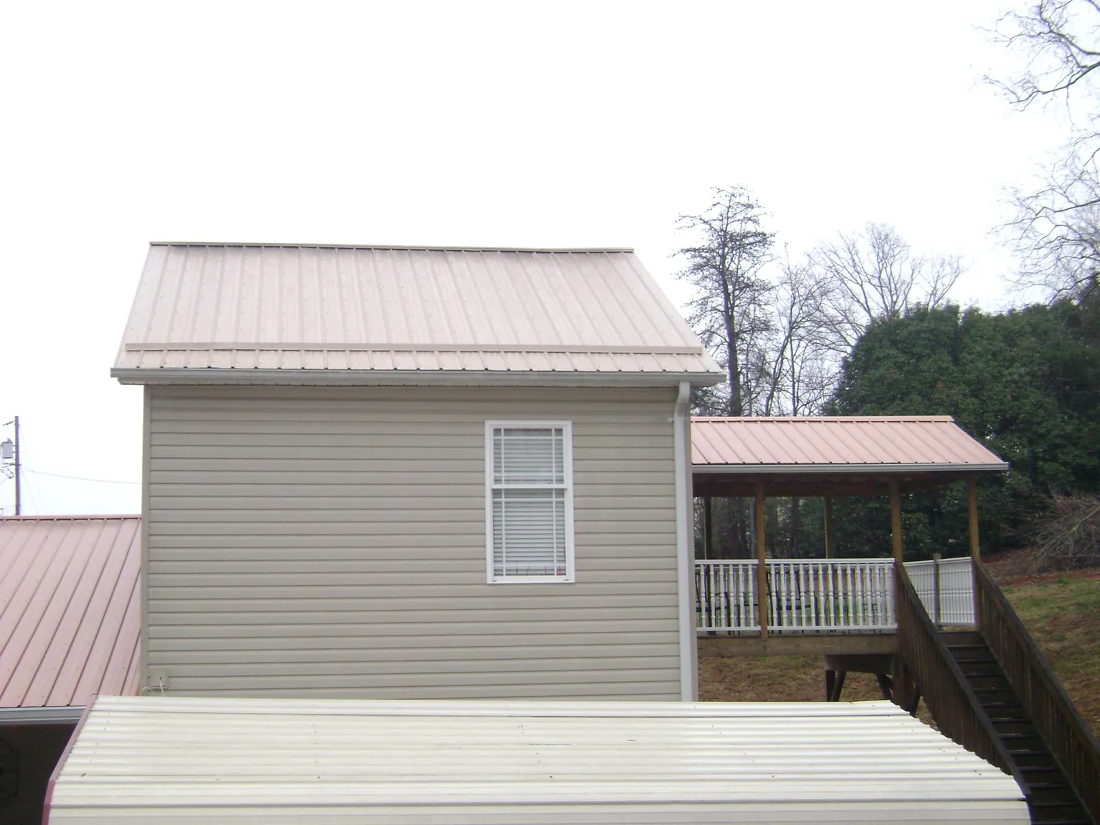 Tan metal roofs on a two story addition and attached porch, from a Roof Replacement job in Rolling Prairie